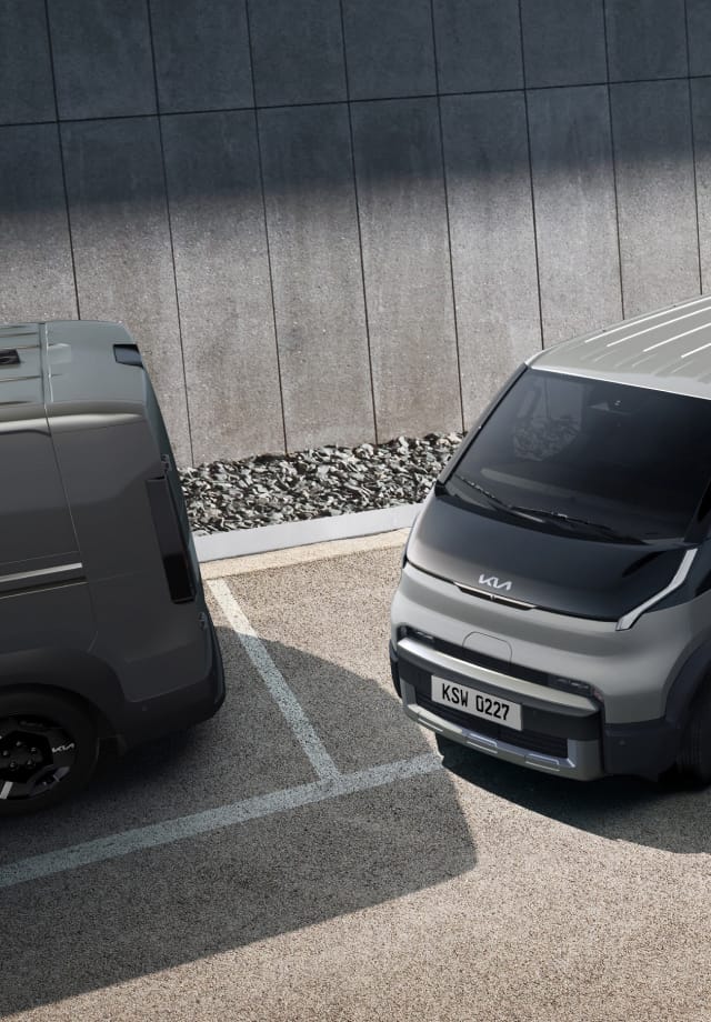 Der Kia PV5 Cargo fährt aus einer Parallelparklücke – auf einem Parkplatz mit zwei weiteren Kleinbussen.